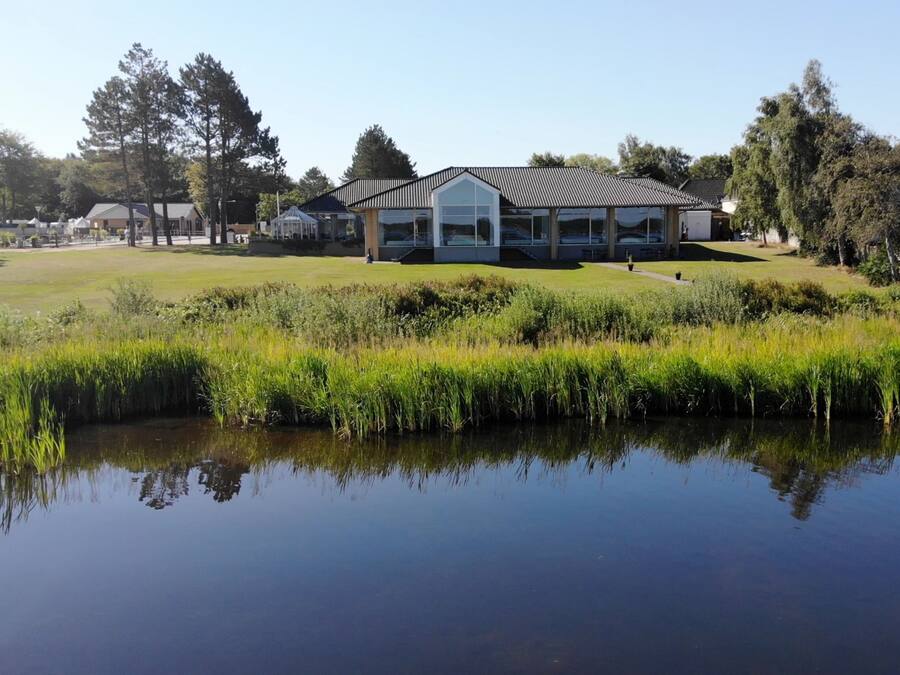 A building with a modern design, surrounded by a well-maintained lawn and a body of water reflecting the structure.