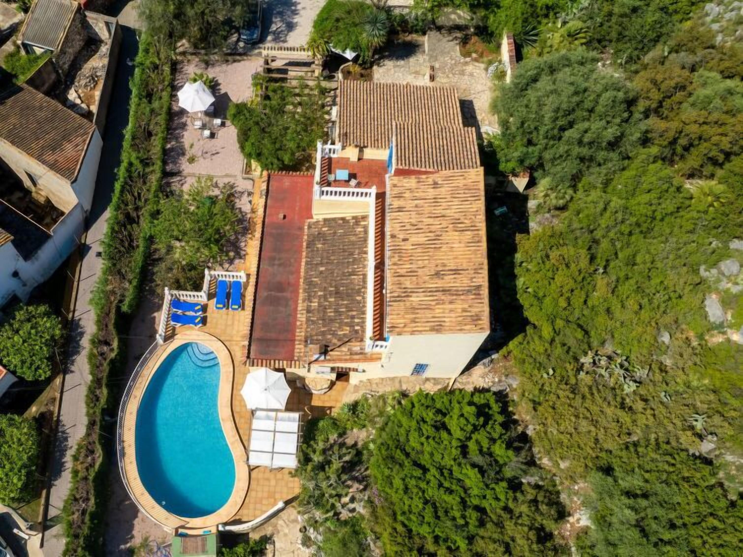 An aerial view of a property with a swimming pool, a covered patio, and a large garden area.