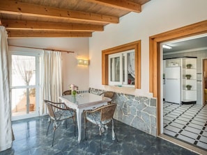 A dining area with a stone wall, wooden ceiling beams, and a view into the kitchen.