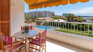 Een balkon met een tafel en stoelen, een zwembad en uitzicht op gebouwen en groen.