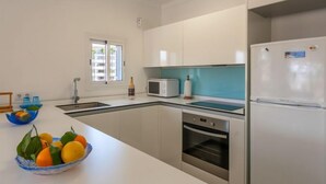 Een moderne keuken met witte kastjes, een inbouwoven, een magnetron en een koelkast.