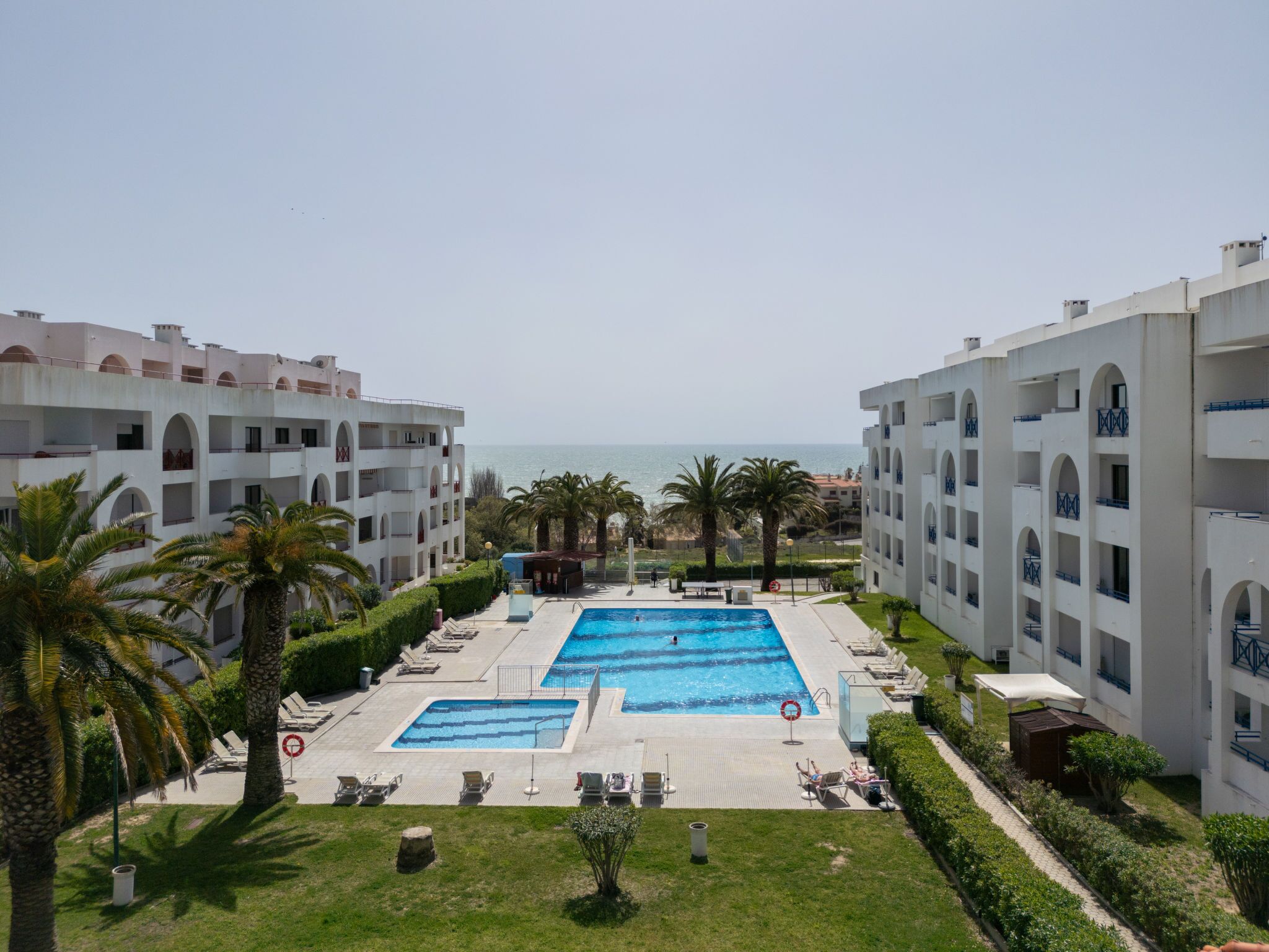 Un resort con piscina central, palmeras y vista al mar.