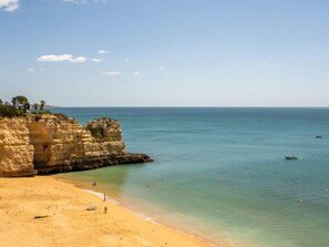 A beach with clear waters, a sandy shore, and rocky cliffs.