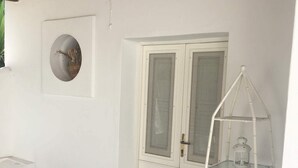 A room with a white door, a white-framed window, a white shelf unit, and a stone floor. - Cottage with large garden in the center of Panarea (Panarea)