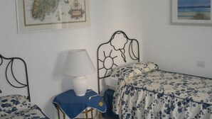 A bedroom with a bed, a chair, a lamp, a map, and a framed picture on the wall. - Cottage with large garden in the center of Panarea (Panarea)