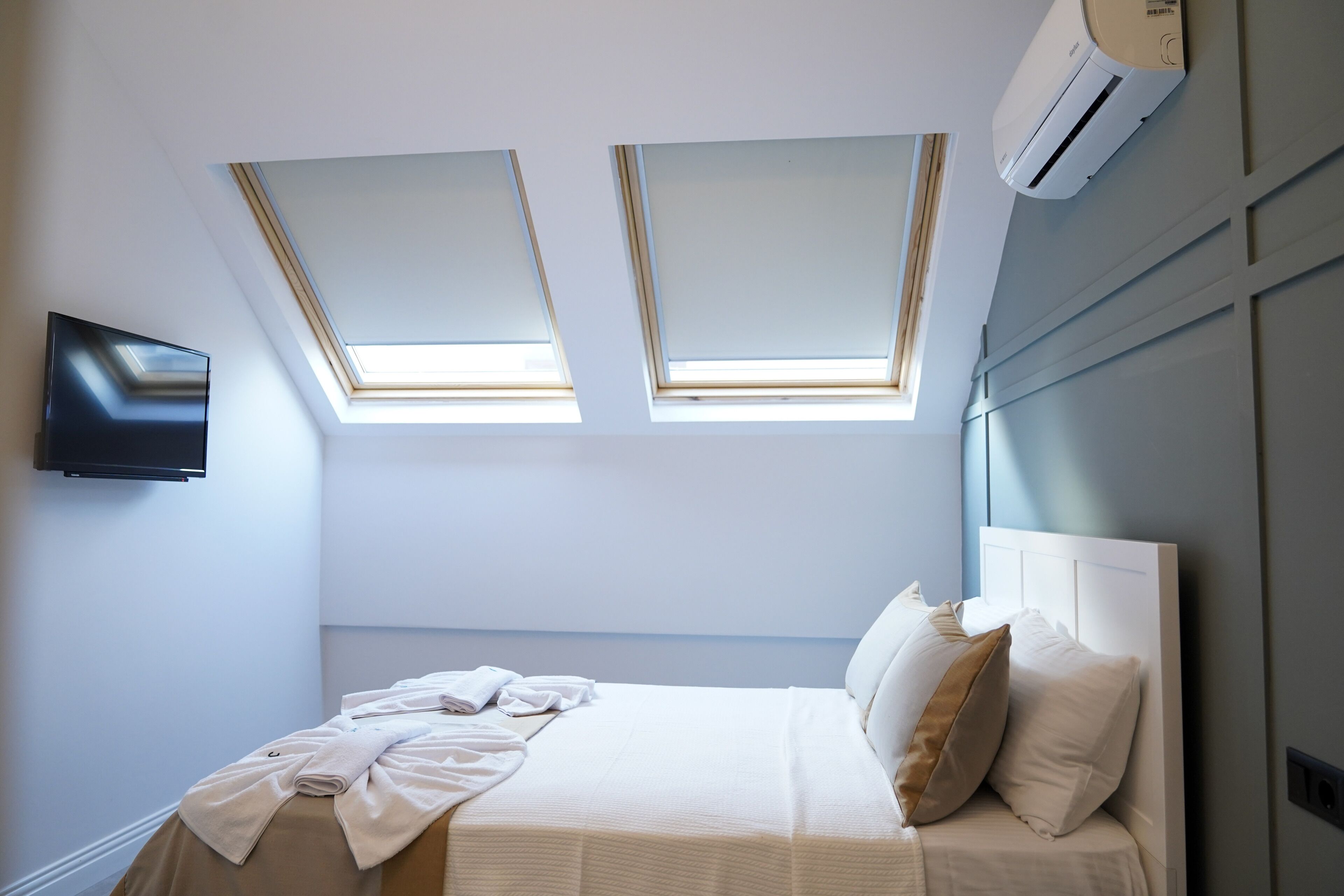 Un dormitorio con cama, dos tragaluces, un televisor de pantalla plana y un equipo de aire acondicionado.