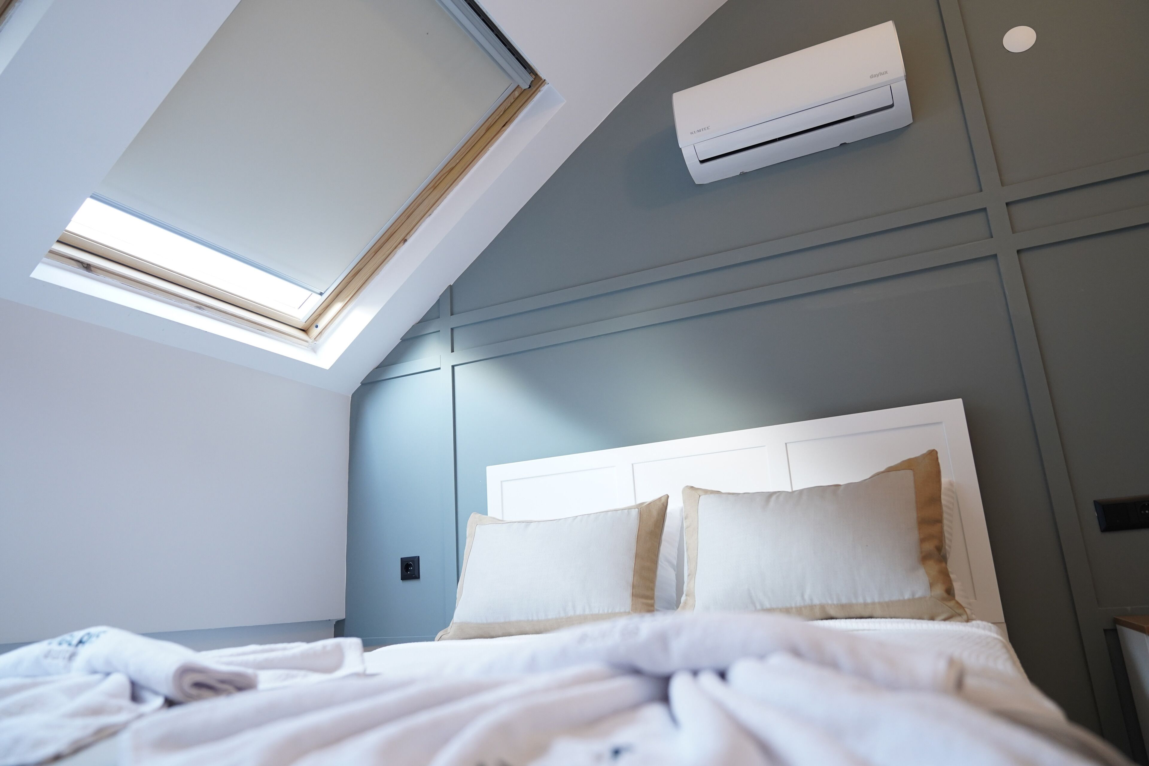 A bedroom with a skylight, a bed with white bedding, and a wall-mounted air conditioner.