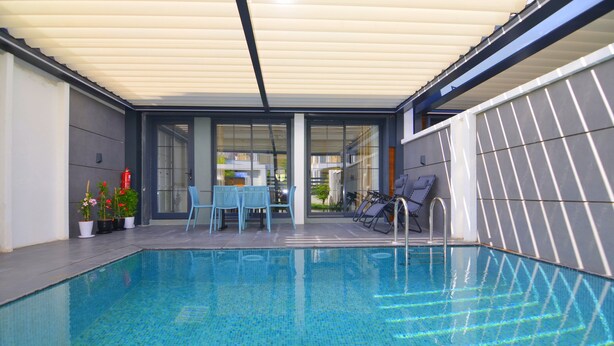 Une piscine intérieure dotée d’un patio couvert, de sièges et de plantes en pot.