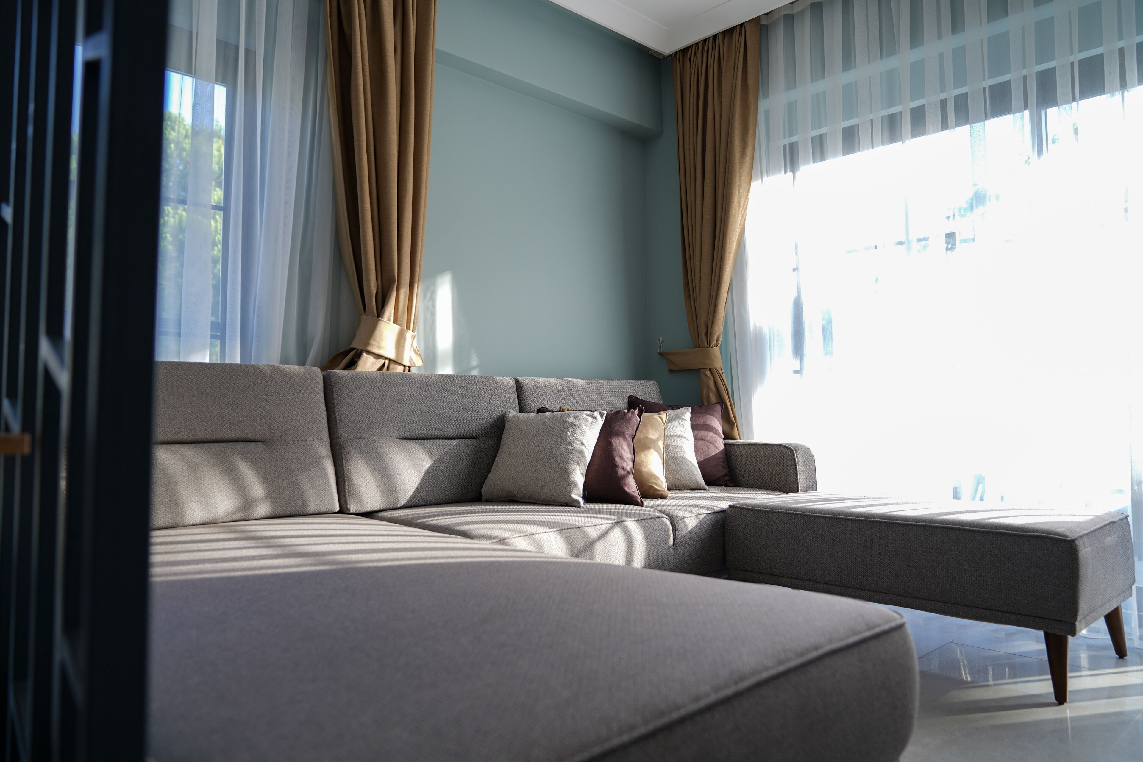 Ein modernes Wohnzimmer mit einer Eckcouch, großen Fenstern und leichten Vorhängen.