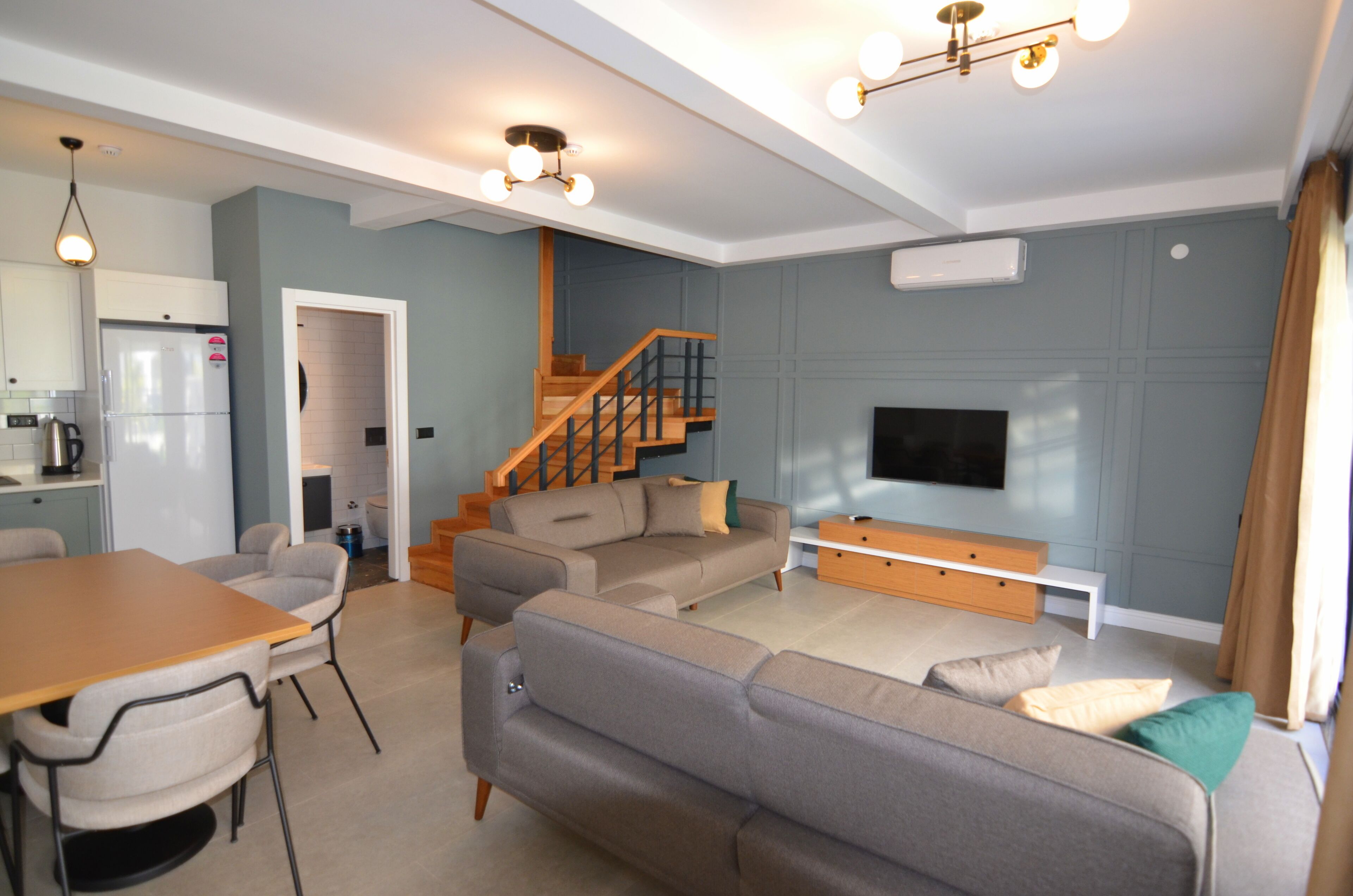 En moderne stue med sofa, spisebord og stole. Der er en trappe, der fører til et andet plan.
