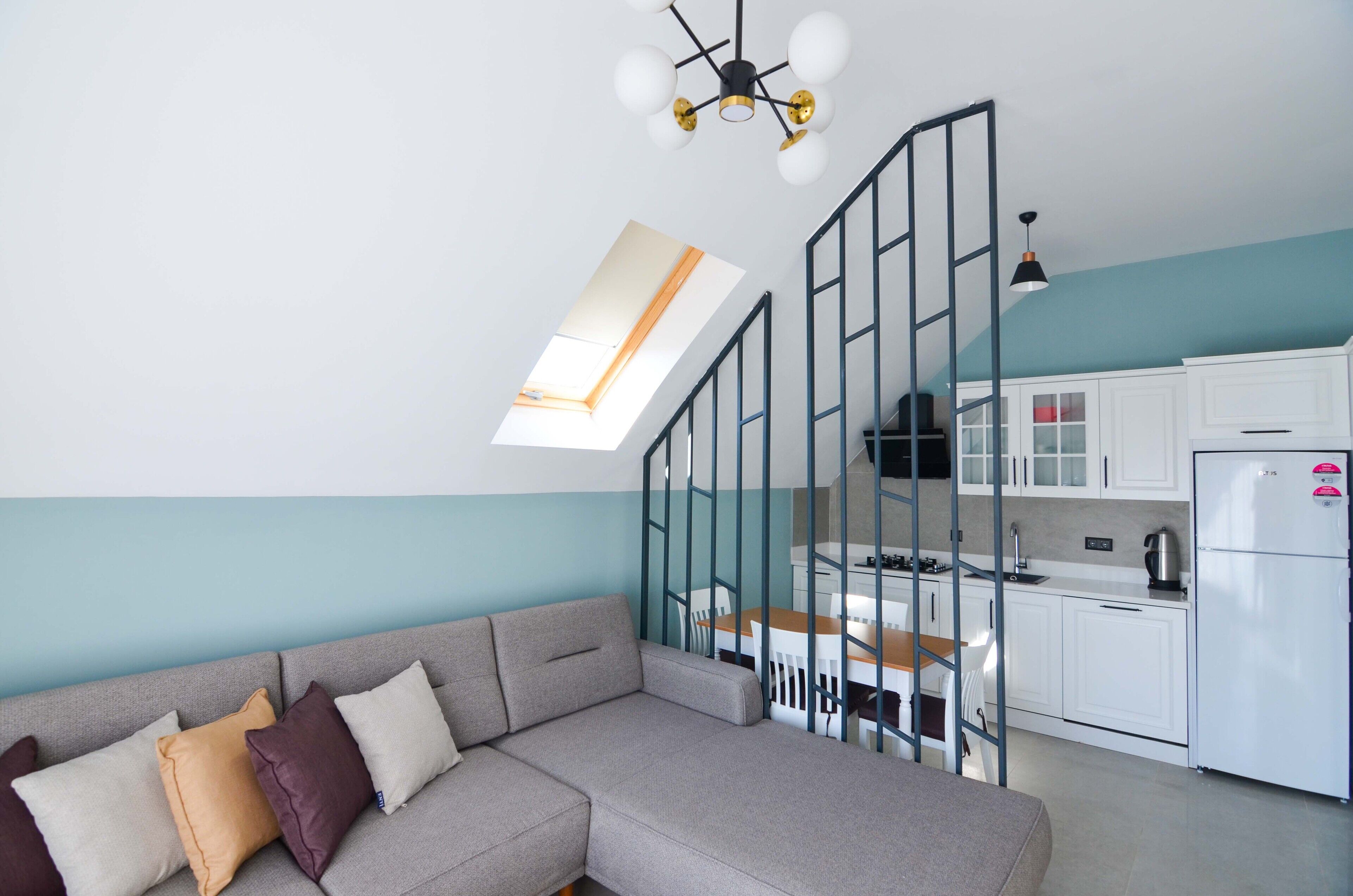 A modern apartment with a grey sofa, a kitchen with white cabinets, and a skylight.
