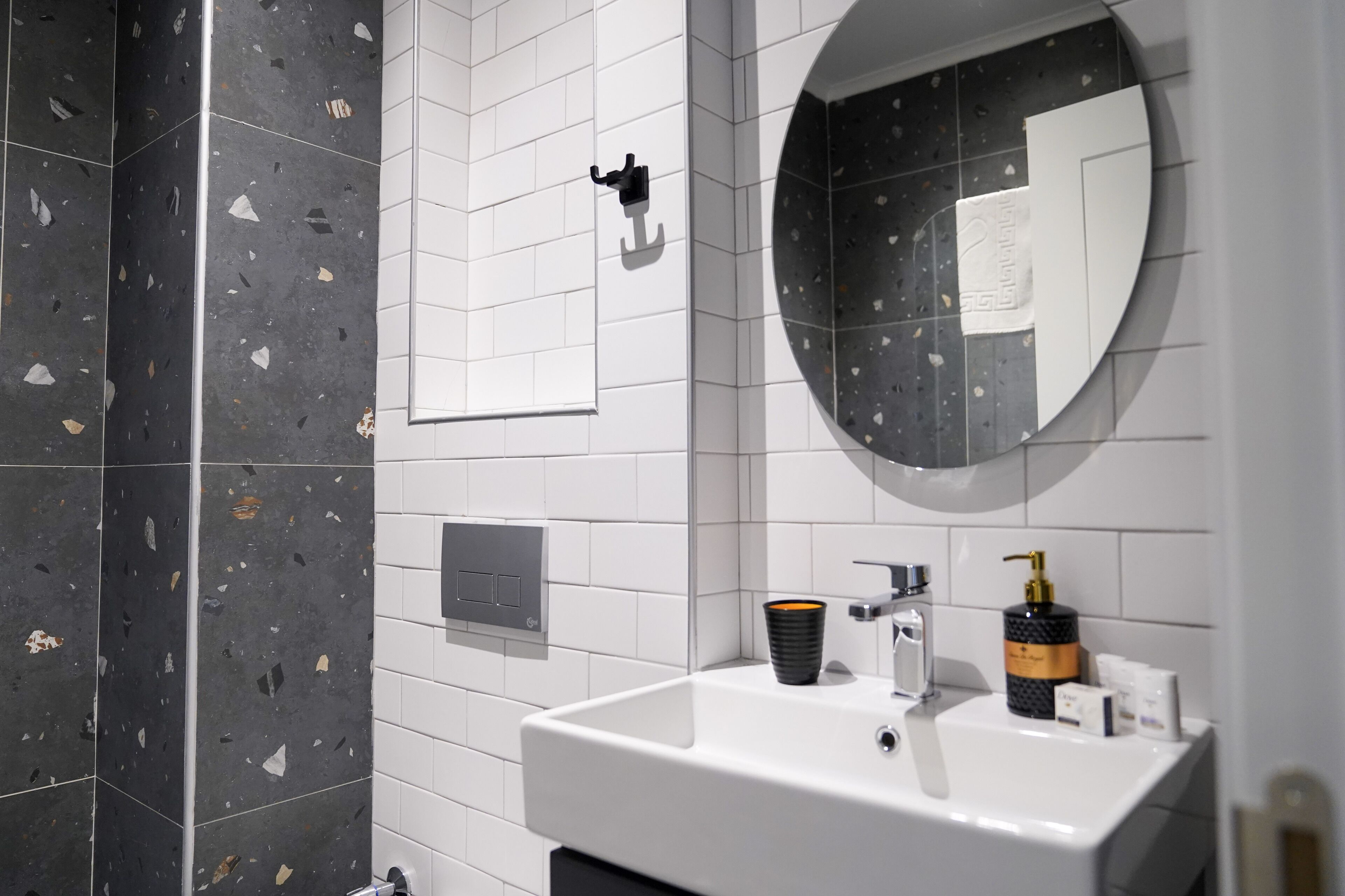 Un baño moderno con un lavabo blanco, un espejo y una pared con azulejos blanco y negro.