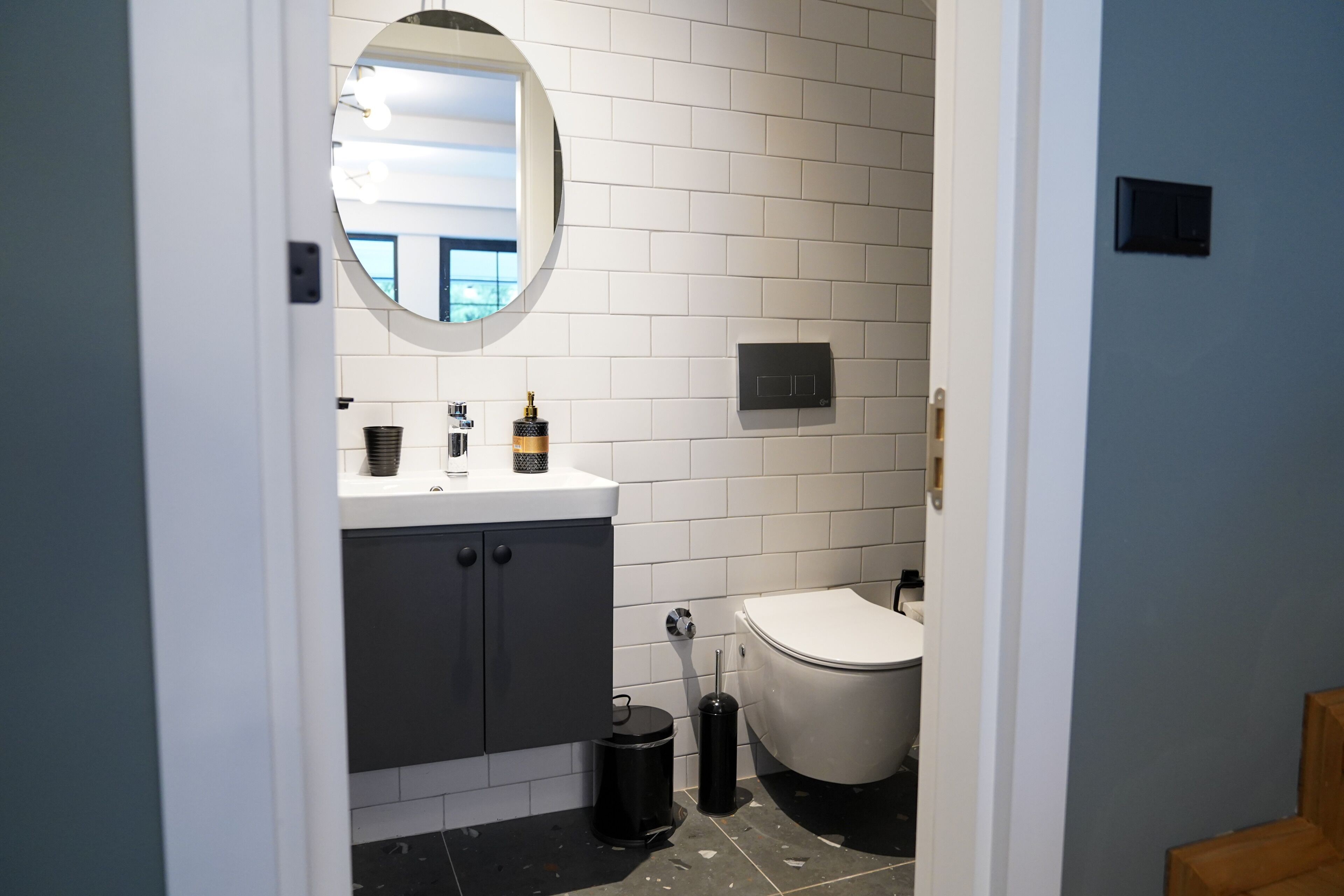 A modern bathroom with white subway tiles, a round mirror, a white sink, and a toilet.