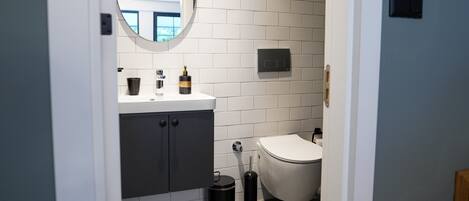 A modern bathroom with white subway tiles, a round mirror, a white sink, and a toilet.