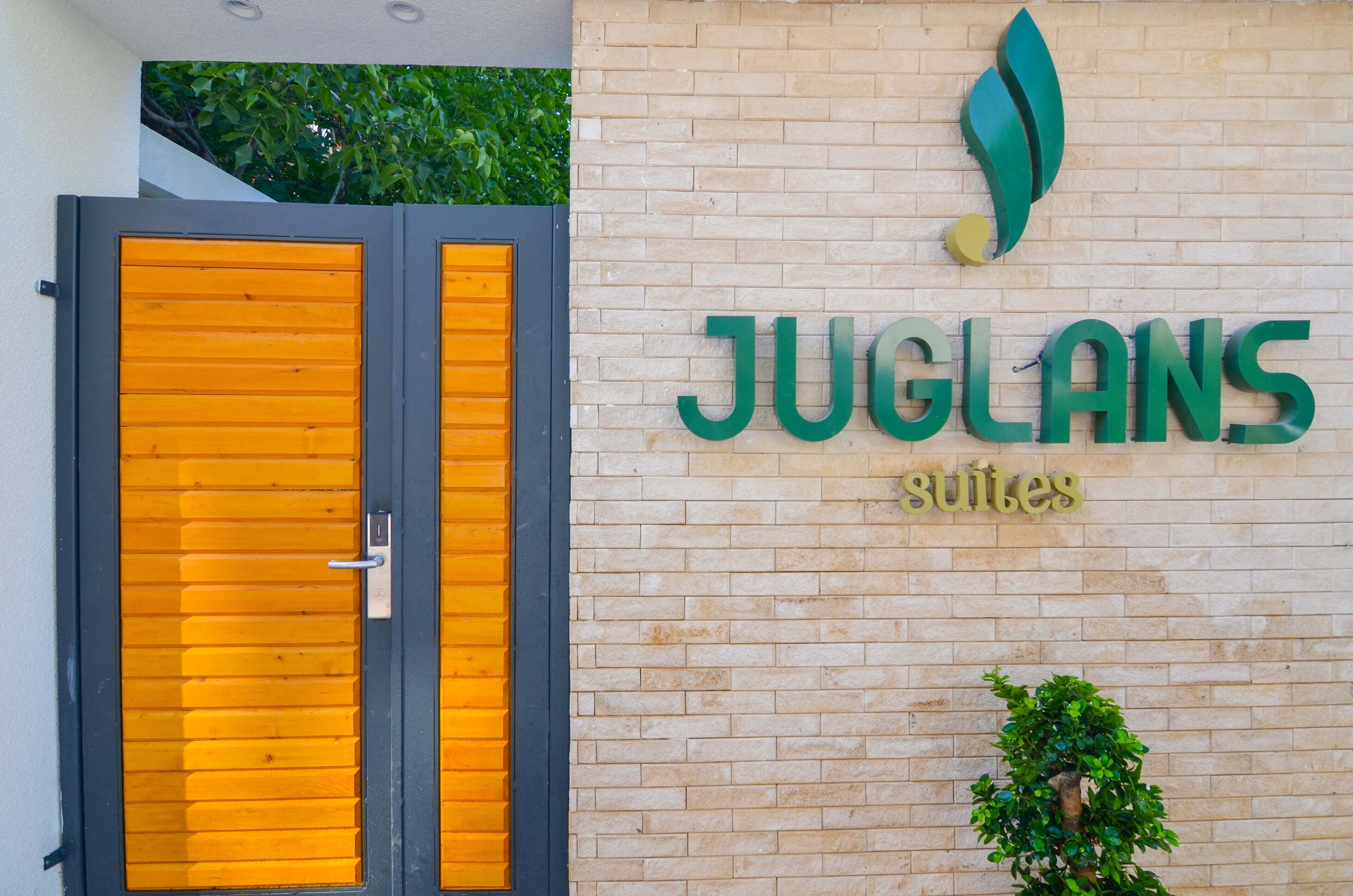 L’entrée d’un hôtel, avec un mur en briques et une enseigne indiquant « JUGLANS suites ».