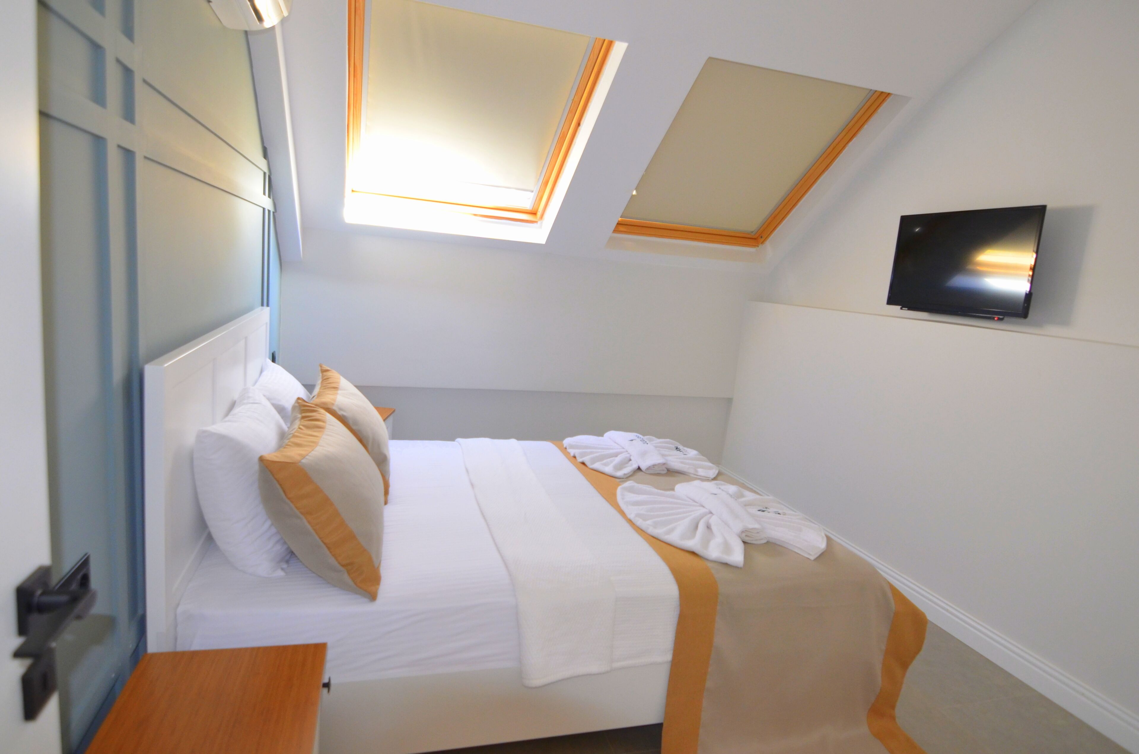 A hotel room with a bed, a TV mounted on the wall, and a window with a view of the sky.