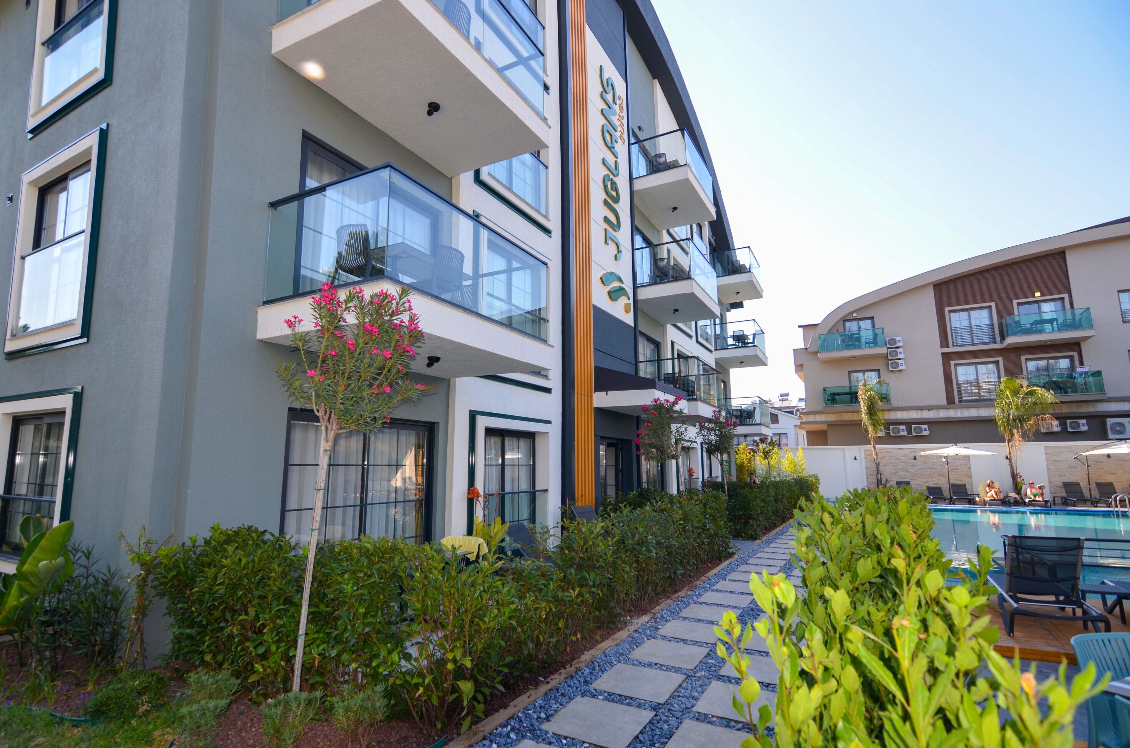 A modern hotel with multiple balconies, a swimming pool, and a well-maintained garden area.