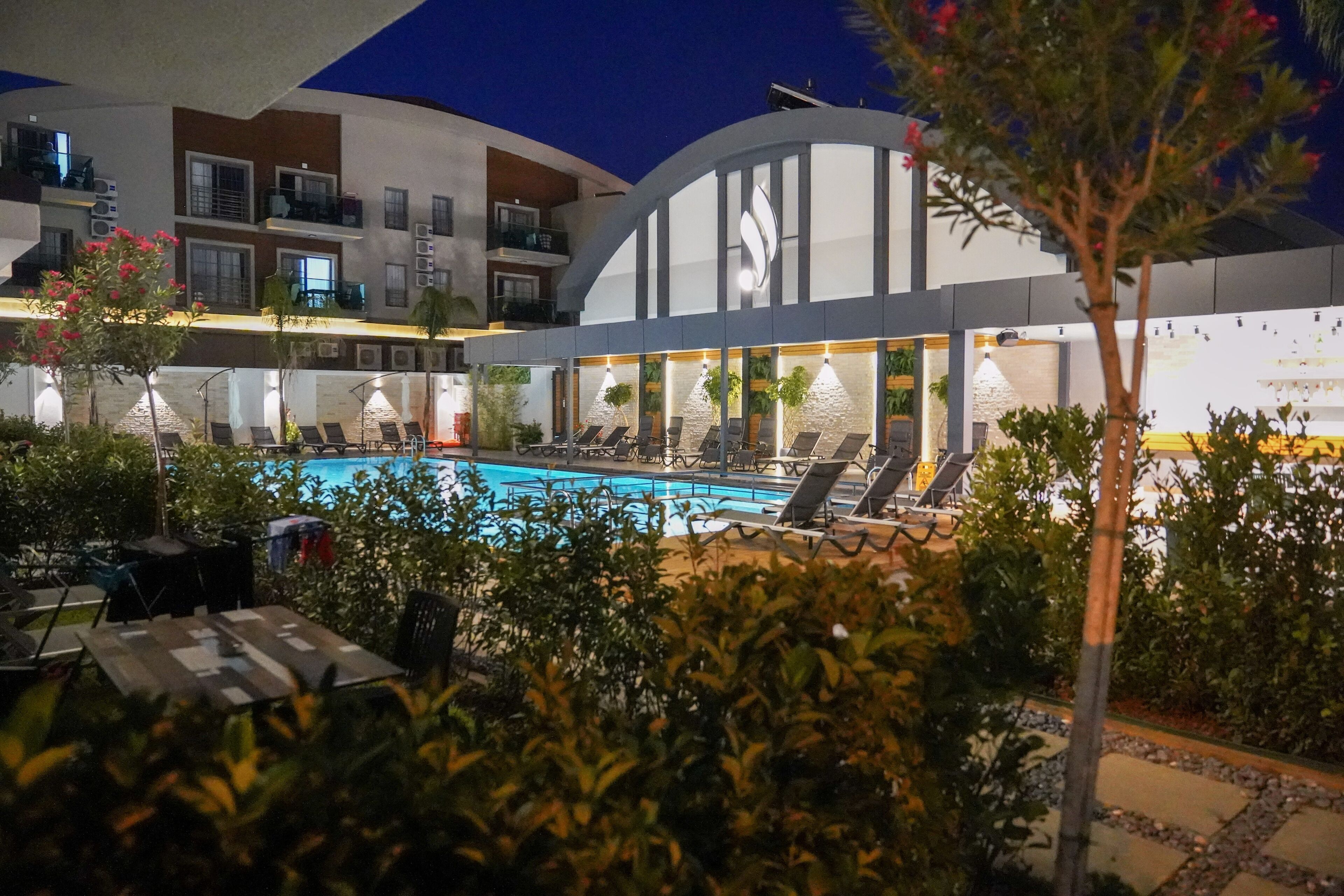 Un hotel con piscina, poltrone a sdraio e una zona esterna ben illuminata.