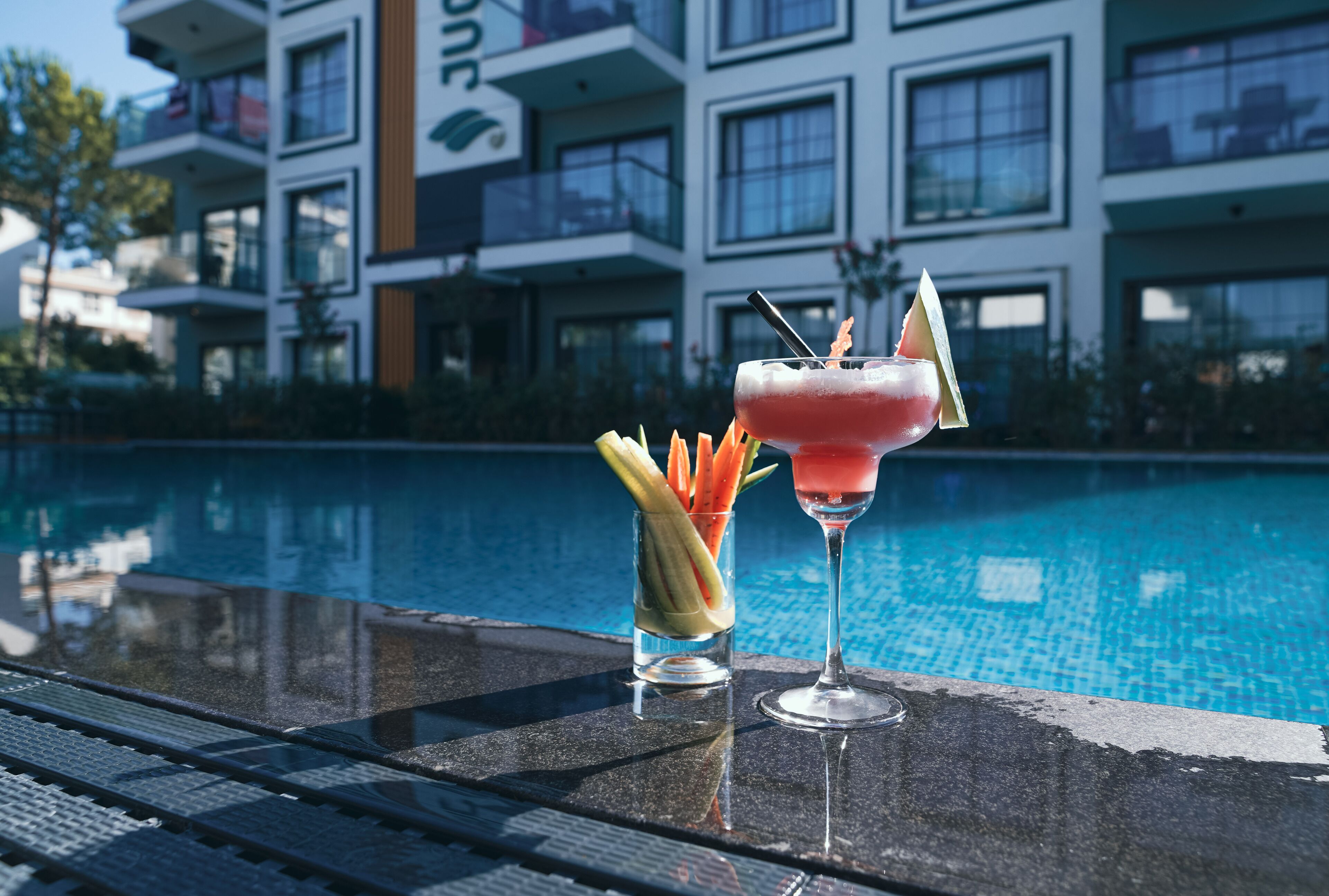 A poolside bar with two cocktails and a glass of fruit.
