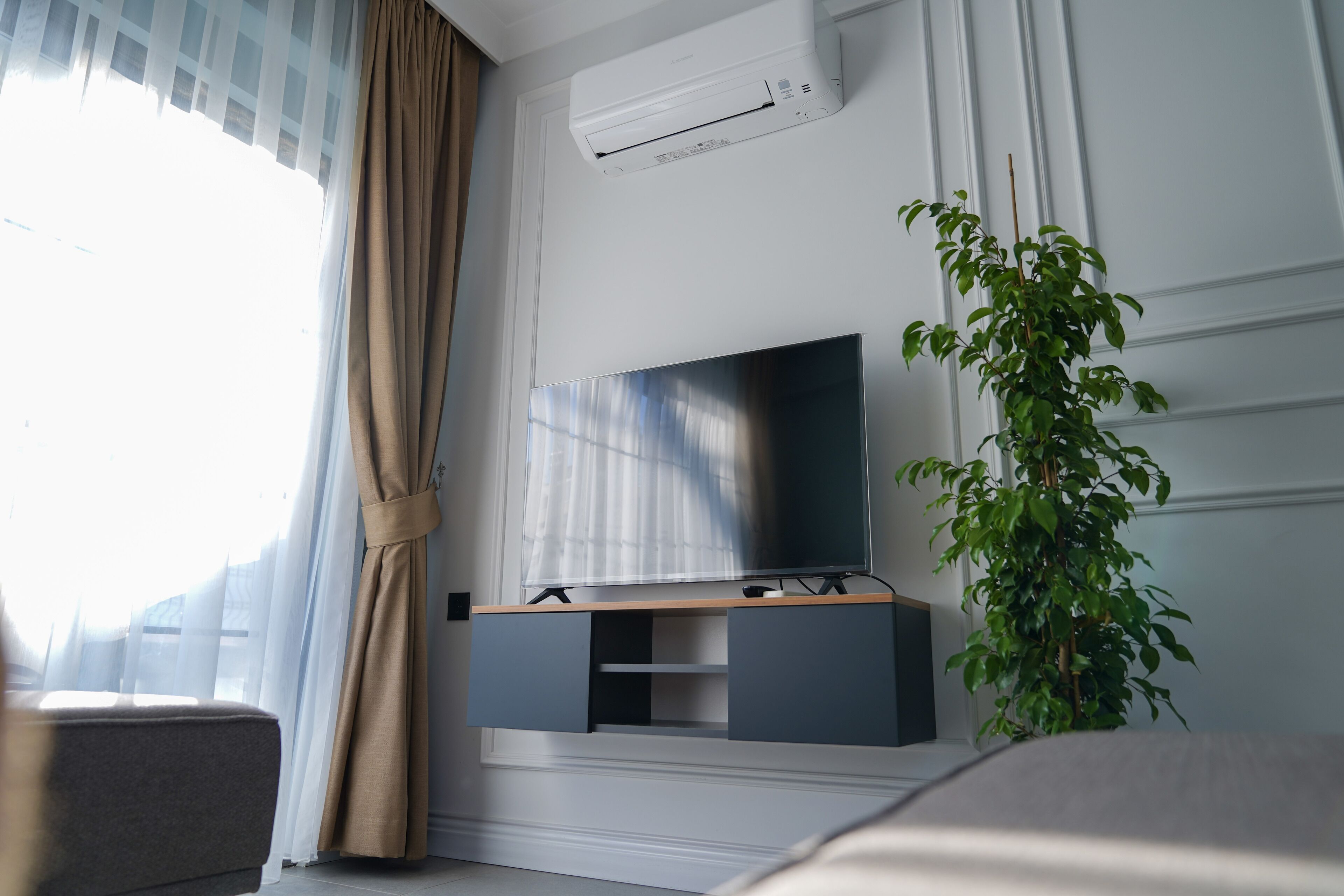 Habitación de hotel moderna con una televisión de pantalla plana en la pared, una planta en maceta y una ventana con cortinas translúcidas.