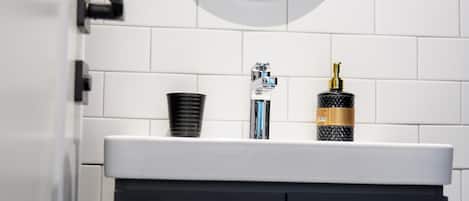 A bathroom with a white tiled wall, a round mirror, a black cabinet with two drawers, and a white countertop.