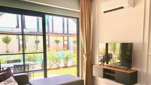 Un salon moderne avec un canapé, un téléviseur posé sur un meuble et de grandes fenêtres donnant sur une piscine et un espace extérieur.