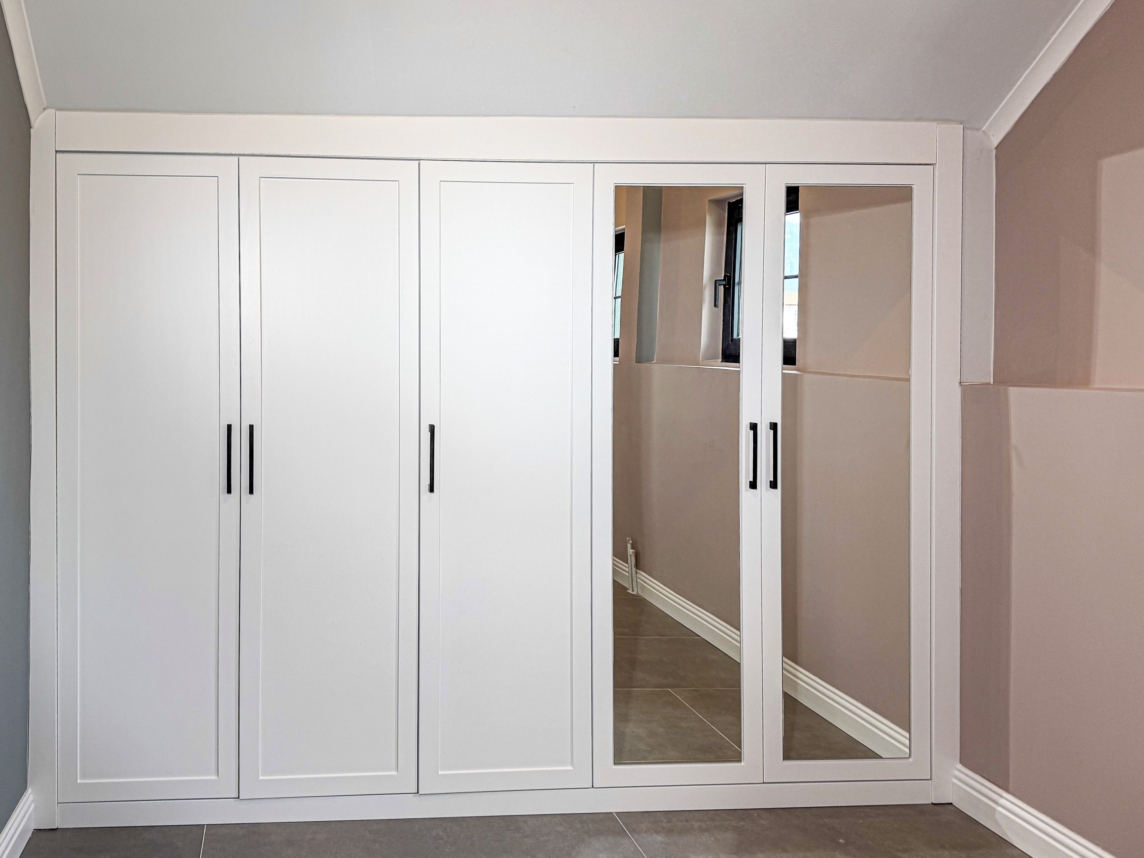 A room with a white wardrobe, a mirrored closet door, and a tiled floor.
