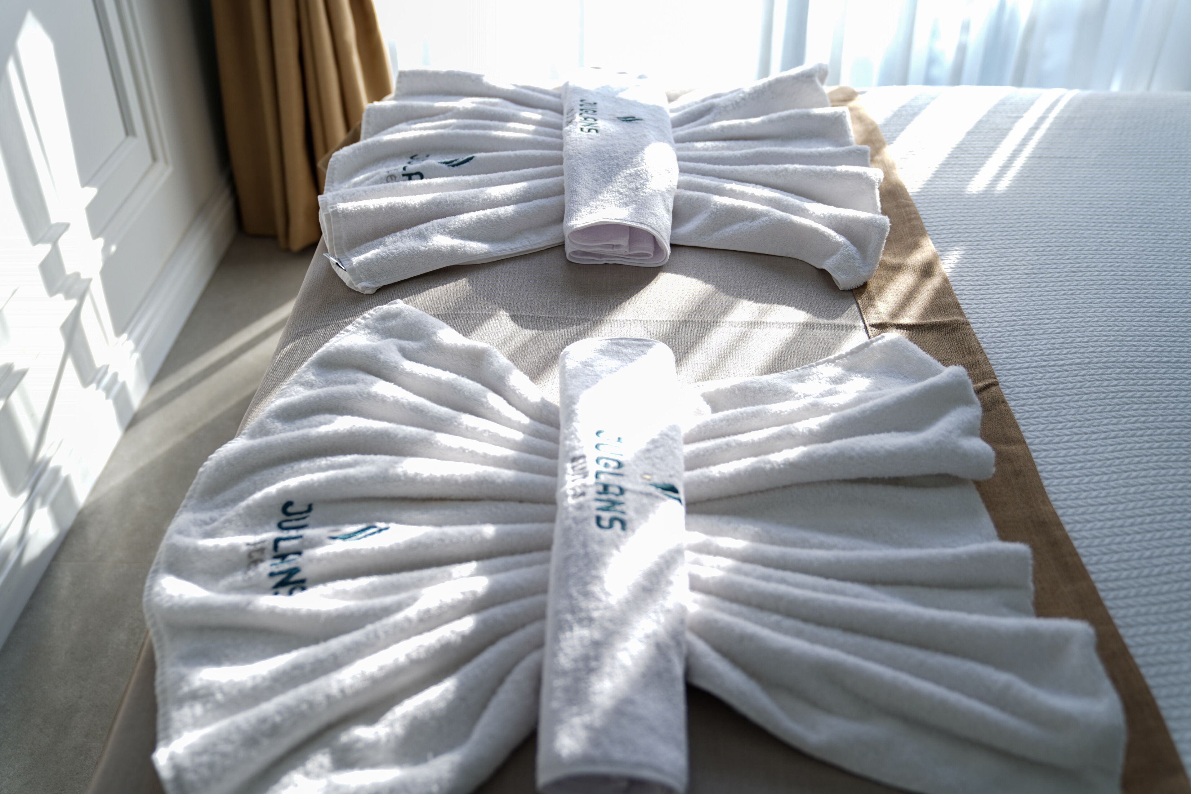 A neatly arranged set of white towels on a bed with a striped pillow and a beige headboard.