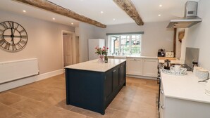 A modern kitchen with a central island, white cabinetry, and a rustic ceiling beam. - Ley Mill Farm (Westbury-on-Severn)