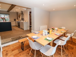 A modern kitchen with a central island, wooden dining table with white chairs, and a view of the adjacent living area.