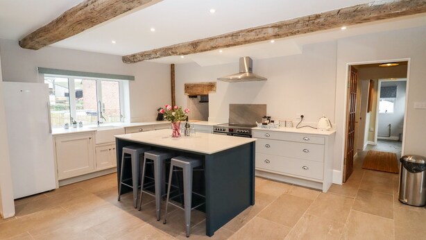 A modern kitchen with a large island, bar stools, a stainless steel stove, and a window providing a view of the outside. - Ley Mill Farm (Westbury-on-Severn)