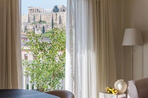 A hotel room with a view of ancient ruins, a potted plant, and a bedside table with a vase and a lamp.