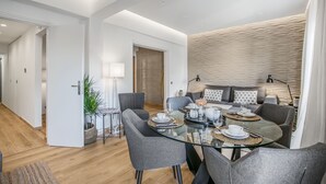 Een moderne eetruimte met een glazen tafel, grijze stoelen en een zithoek.
