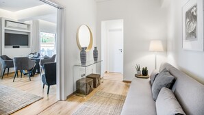 Een moderne woonkamer met een glazen salontafel, een grijze bank en een eethoek met stoelen en een televisie.