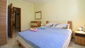 A bedroom with a bed, a nightstand, a dresser, a mirror, and a door leading to another room.