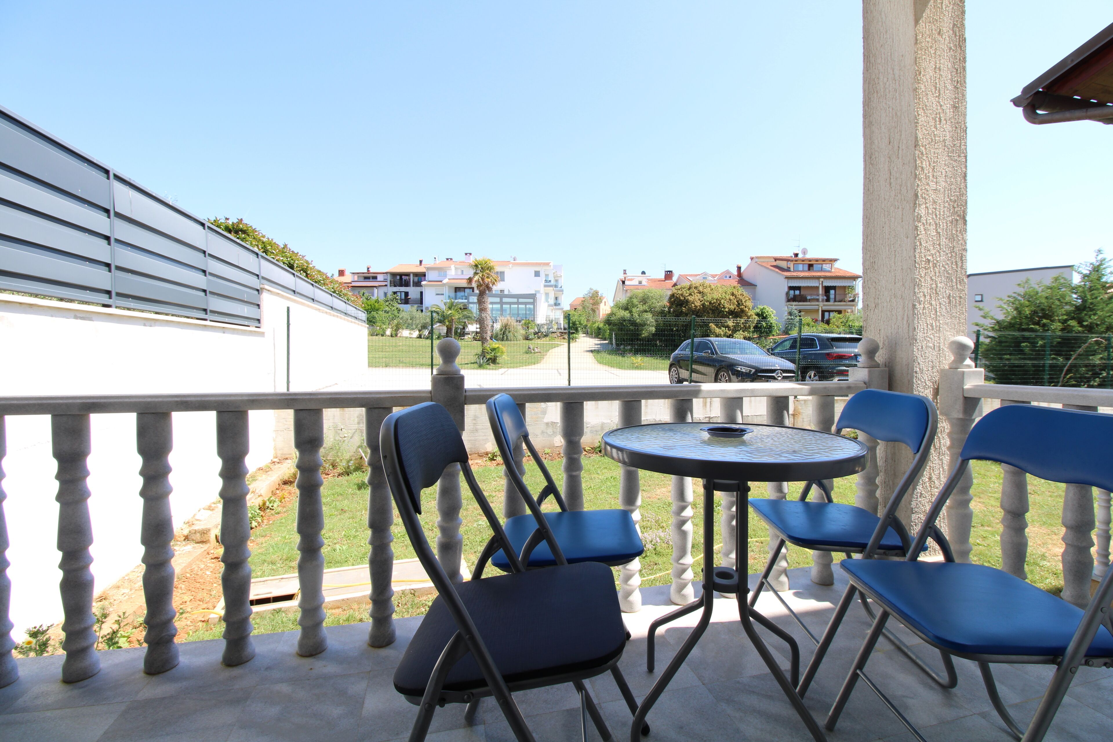 A balcony with a table and chairs, a view of a residential area, and a clear sky.