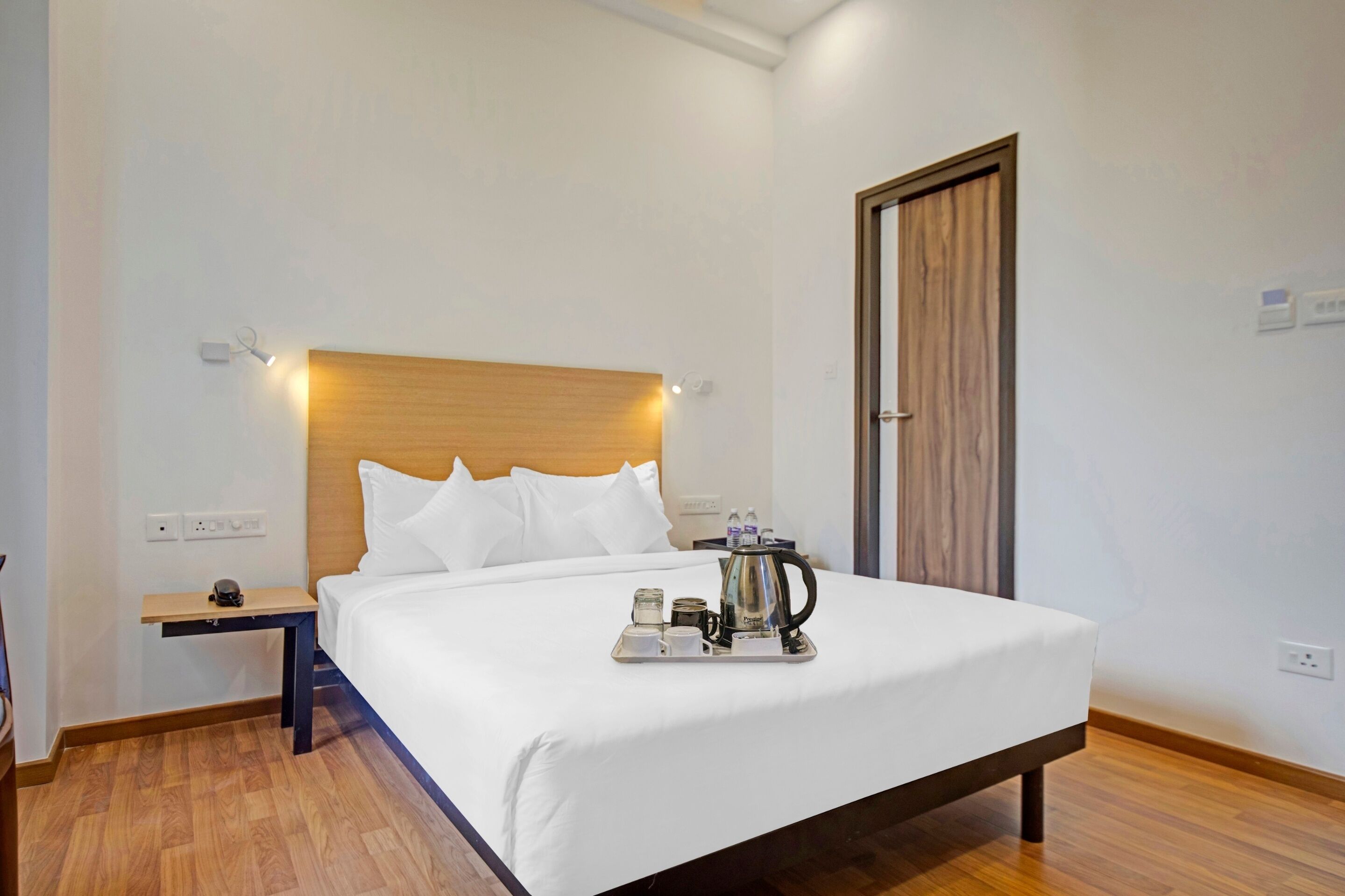 A neatly made bed with white linens, a wooden headboard, and a tray with cups and a kettle.