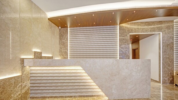Un espace d’accueil moderne avec un sol en marbre, un plafond incurvé et un escalier menant à un niveau supérieur.