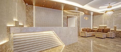 A modern lobby with a marble reception desk, a sofa area, and a chandelier.