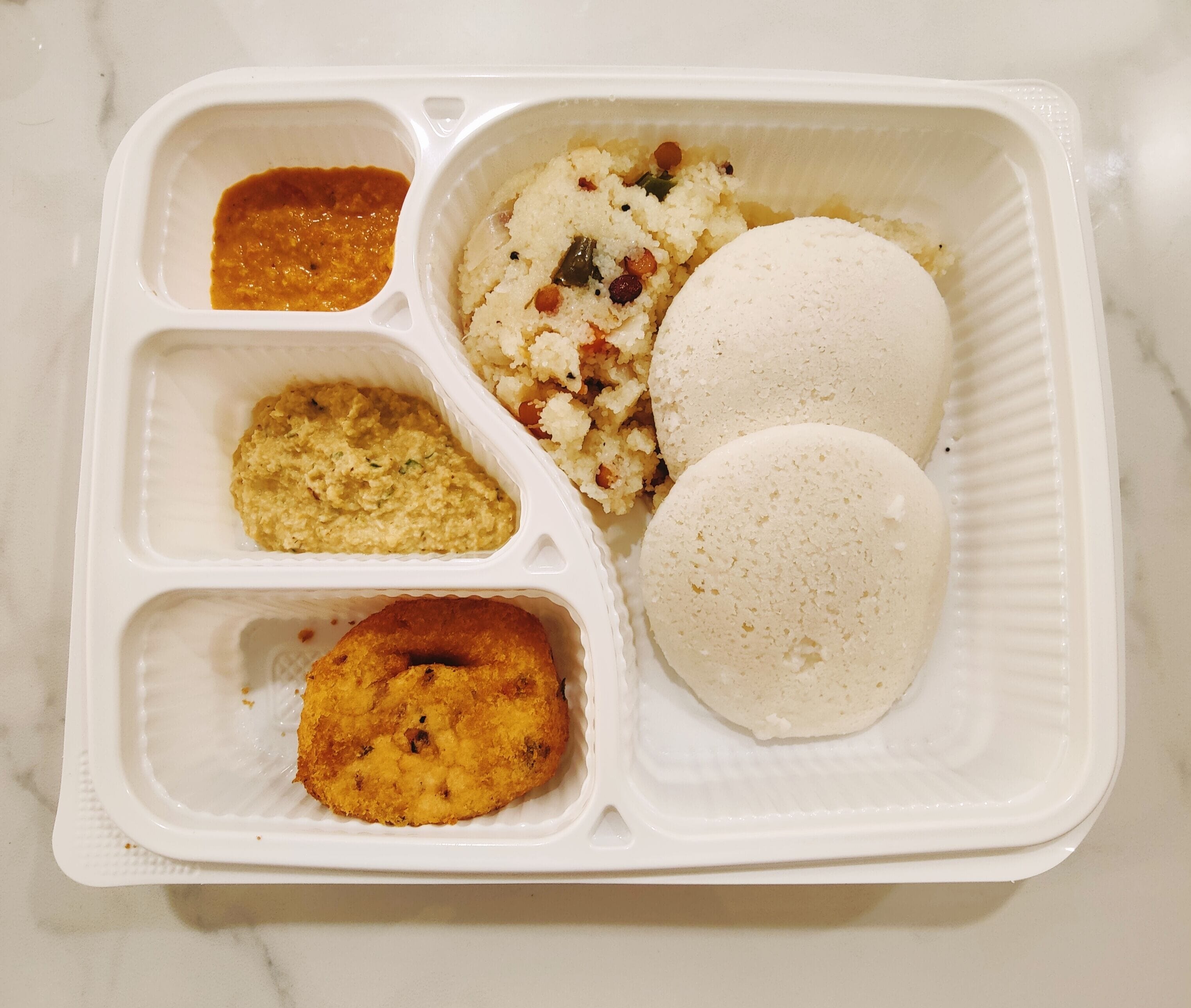 A meal in a compartmentalized takeout container with rice, a fried item, and two types of sauces.