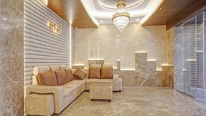 Un hall d’entrée luxueux, avec un canapé d’angle, un petit pouf, un sol en marbre et un lustre.
