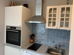 A kitchen with white cabinets, a stainless steel range hood, a black oven, a sink, and a backsplash with blue tiles.