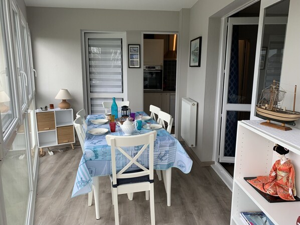 A dining area with a table set for four, a white chair, a small cabinet, and a radiator.