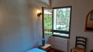 A bedroom with a bed, a small bedside table, a chair, a window with a view of greenery, and a wall-mounted light fixture. - Family Villa with Terrace, Near Beach and Shops in Seignosse (Seignosse)