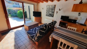 A cozy room with a sofa, a dining table, and a TV. There's a sliding glass door leading to a garden. - Family Villa with Terrace, Near Beach and Shops in Seignosse (Seignosse)