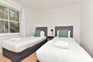 A hotel room with two beds, a window, and a nightstand with a lamp.