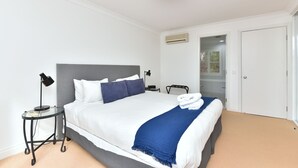 A hotel room with a bed, bedside table, lamp, and an air conditioning unit.