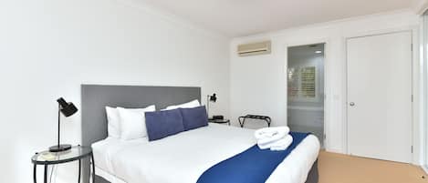 Una habitación de hotel con una cama, mesita de noche, lámpara y un equipo de aire acondicionado.
