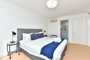 A hotel room with a bed, bedside table, lamp, and an air conditioning unit.