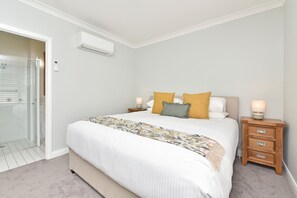 A bedroom with a bed, bedside tables, a nightstand, a wall-mounted air conditioner, and a glass shower enclosure.